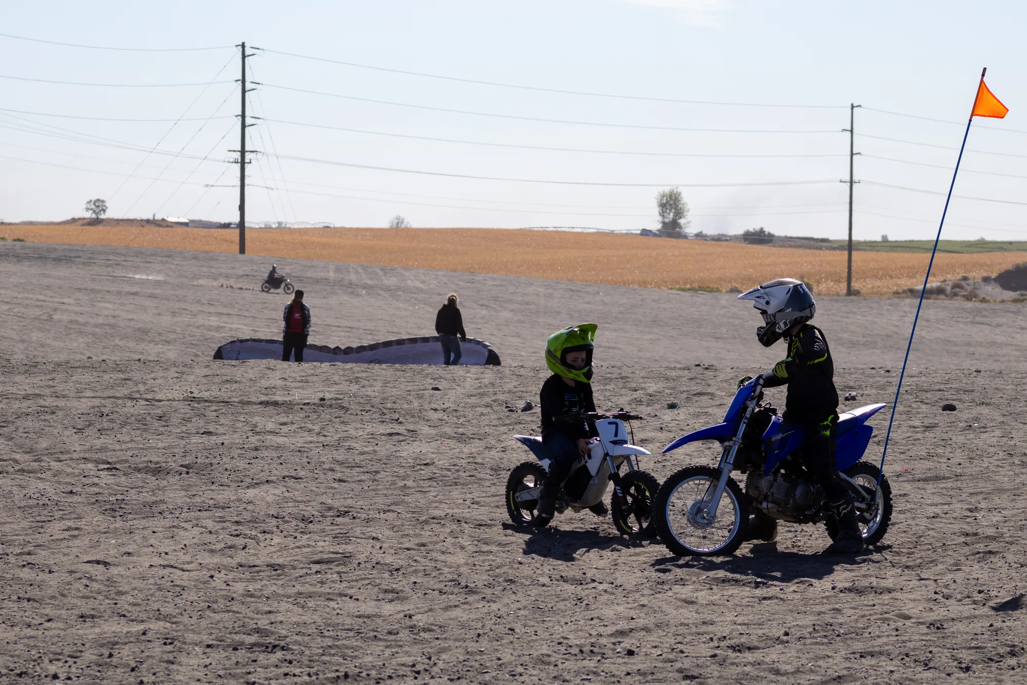 Kids on dirt bikes with a paramotor wing laid out in the background