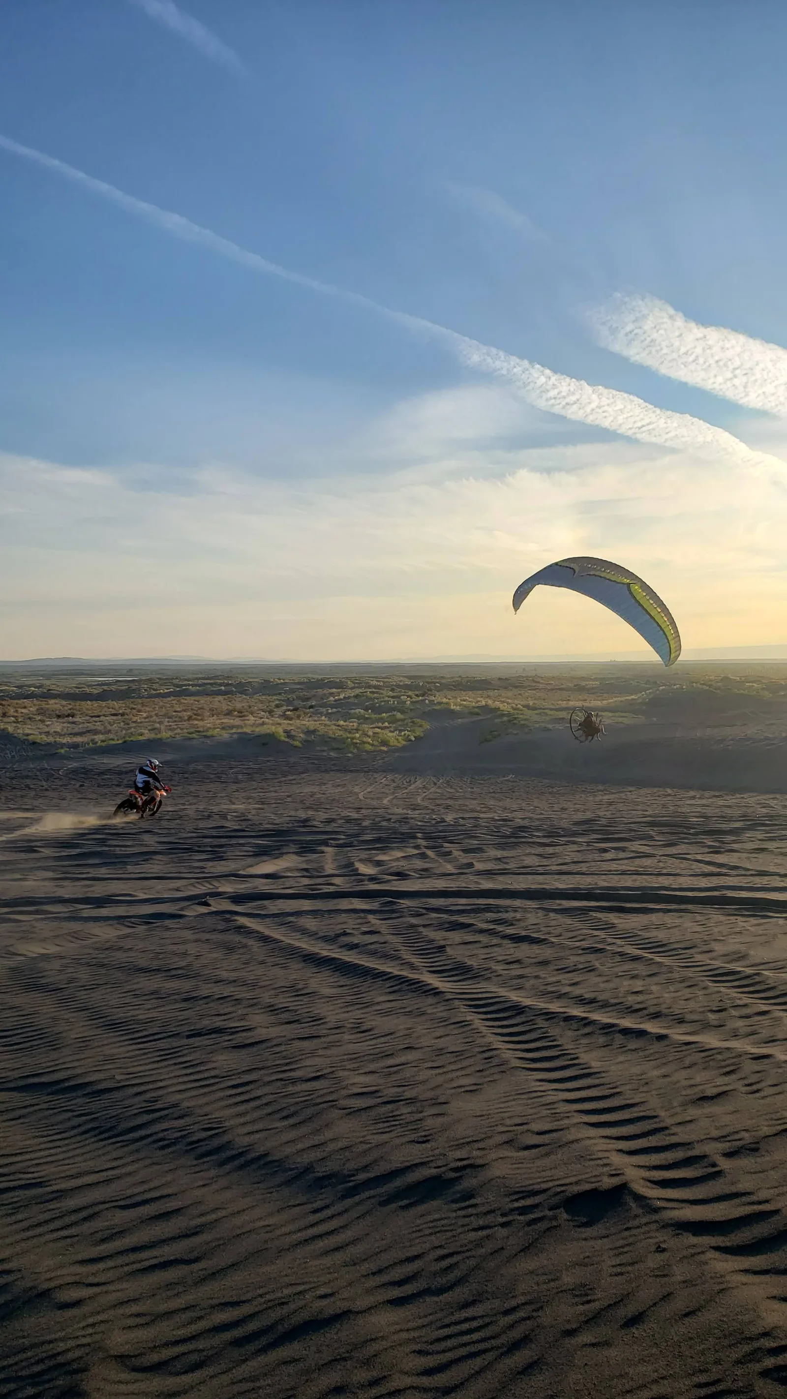 Rider giving a shaka with a paramotor flying above at sunset